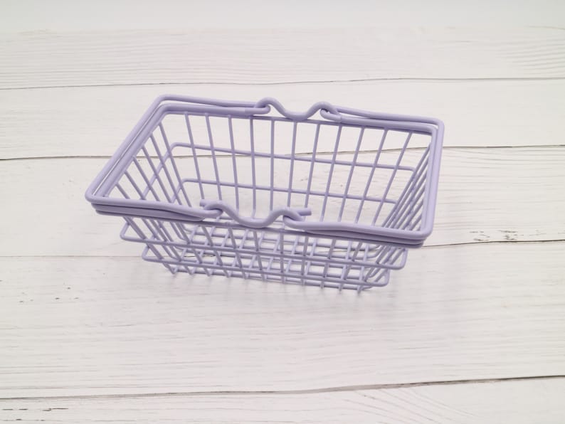 Puede incluir: Una cesta de la compra de alambre lavanda con un asa sobre una superficie de madera blanca.