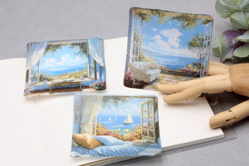 May include: Three rectangular art pieces depicting scenic coastal views. Each piece showcases a window or open space with a blue sky, ocean, and lush greenery. One features a sailboat, another a patio with a white couch, and the third a table.