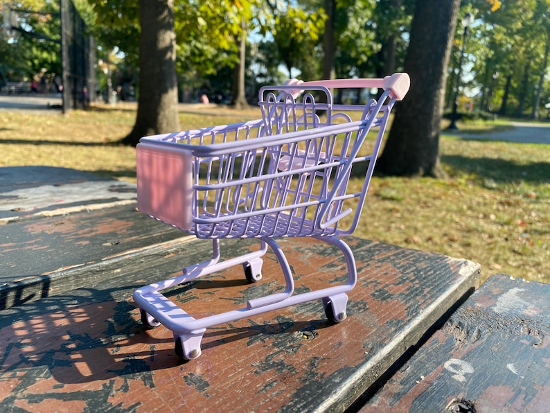 Puede incluir: Un carrito de la compra en miniatura de color morado con un forro rosa sobre una superficie de madera.
