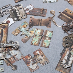 May include: A collection of assorted metal hardware components including various hinges, drawer pulls, and decorative plates. The items feature weathered, rusted, and oxidized finishes in shades of brown, metallic silver, and aged green patina.