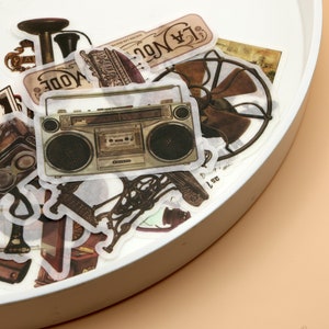 Könnte beinhalten: Eine Sammlung von Vintage-Aufklebern mit einem Retro-Boombox, einer Kamera, einem Ventilator und verschiedenen anderen Designs. Die Aufkleber befinden sich auf einem weißen Hintergrund.