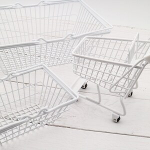 May include: Three white wire baskets, one is a shopping cart with wheels, the other two are rectangular with handles.