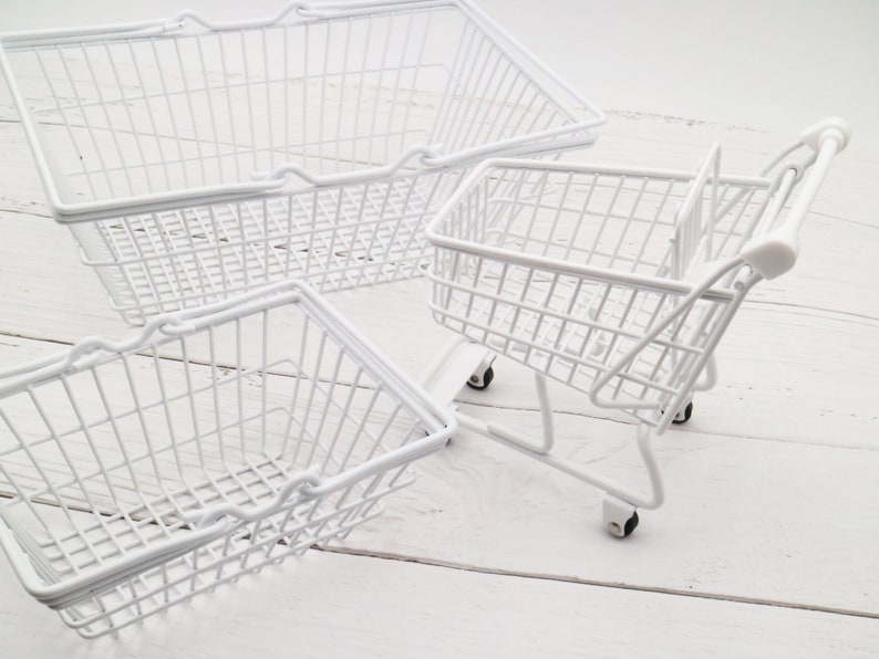 May include: Three white wire baskets, one is a shopping cart with wheels, the other two are rectangular with handles.