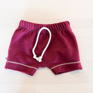 May include: Burgundy red shorts with a white drawstring and white stitching around the edges.