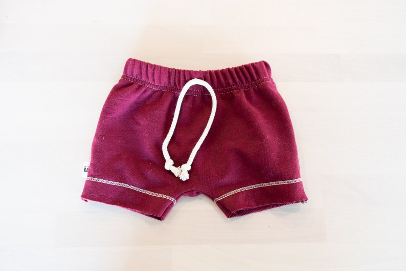 May include: Burgundy red shorts with a white drawstring and white stitching around the edges.