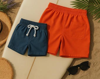 Peut inclure: Deux paires de shorts de bain, l'un bleu et l'autre orange, disposés sur une planche de surf.