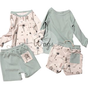 Puede incluir: Un conjunto de ropa para niños de cuatro piezas con temática de playa. El conjunto incluye una camisa de manga larga con fondo blanco y estampado de palmeras y tablas de surf, una camisa de manga larga de color azul claro sólido, un par de pantalones cortos de color azul claro con un bolsillo y un par de pantalones cortos blancos con estampado de palmeras y tablas de surf.