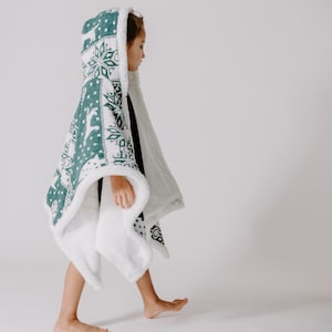May include: A white hooded blanket with a green snowflake and reindeer pattern. The blanket is made of soft, plush fabric and is perfect for keeping warm on cold days.