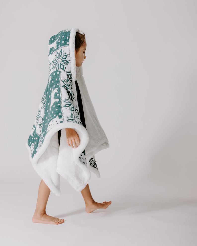 May include: A white hooded blanket with a green snowflake and reindeer pattern. The blanket is made of soft, plush fabric and is perfect for keeping warm on cold days.