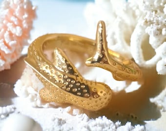 May include: A gold-toned ring featuring a whale shark design. The ring is detailed with a textured surface and a curled tail.