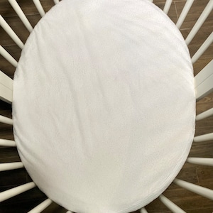 Op de afbeelding: Witte ronde wiegmatras met een wit houten wiegframe.