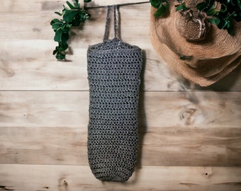 May include: A gray crocheted reusable grocery bag hanging on a wooden surface.