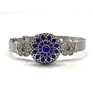 May include: A silver bracelet with a blue and silver charm. The charm is a round, ornate design with blue rhinestones. The bracelet is made of a mesh metal.