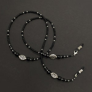 May include: Black beaded eyeglass chain with silver oval charms. The chain has two loops at each end for attaching to glasses.