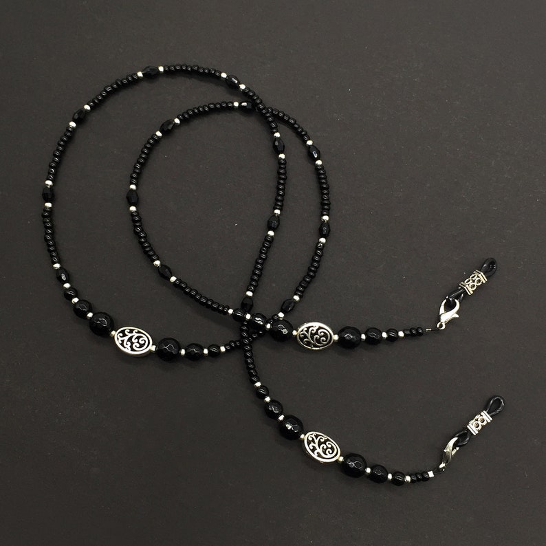 May include: Black beaded eyeglass chain with silver oval charms. The chain has two loops at each end for attaching to glasses.