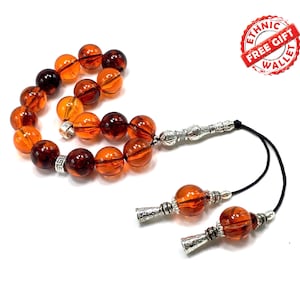 May include: A brown and orange amber prayer beads with silver accents. The beads are strung on a black cord with silver tassels. The image includes the text "Ethnic Free Gift Wallet".