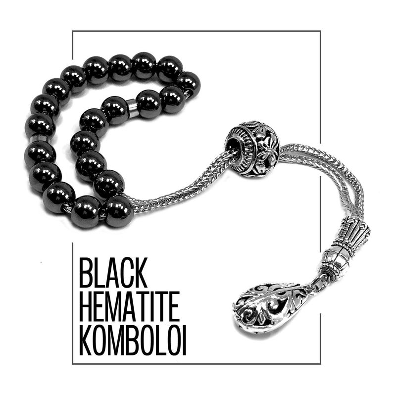 Puede incluir: Un komboloi de hematita negra, un tipo de cuentas de preocupaci&oacute;n, con una cadena plateada y una pieza final decorativa. Las cuentas son redondas y pulidas, reflejando la luz. El texto "BLACK HEMATITE KOMBOLOI" se muestra en negrita.
