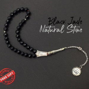 May include: Black jade natural stone prayer beads with a silver tassel and a silver charm with Arabic calligraphy. The beads are strung on a silver chain.