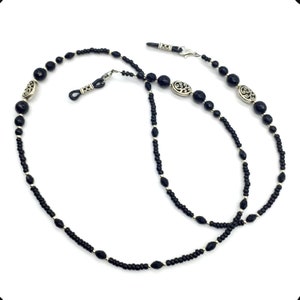 May include: Black beaded eyeglass chain with silver accents. The chain has small black beads and larger black beads with silver filigree designs.