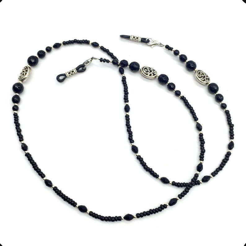 May include: Black beaded eyeglass chain with silver accents. The chain has small black beads and larger black beads with silver filigree designs.