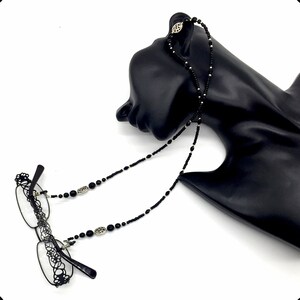 May include: Black beaded eyeglass chain with silver accents. The chain is displayed on a black mannequin head.