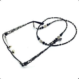 May include: Black beaded eyeglass chain with silver-toned charms. The chain is made of small black beads and features a decorative metal design. The chain is attached to the glasses with two small metal clips.