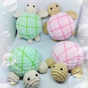 May include: Four crocheted turtle toys in shades of green, pink, and beige. The turtles have a grid pattern on their shells and small, round heads with button eyes. The toys are soft and plush.