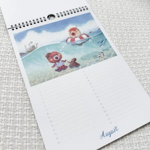 K&ouml;nnte beinhalten: Ein Spiral-Kalender mit einer Illustration von Cartoon-Oktopussen im Meer. Ein Oktopus befindet sich in einem rot-wei&szlig; gestreiften Schwimmring, ein anderer tr&auml;gt ein gestreiftes Hemd. Das Wort "August" ist blau geschrieben.