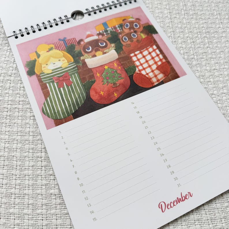 K&ouml;nnte beinhalten: Ein Spiral-Kalender mit einer Dezemberseite mit Illustrationen von Cartoon-Charakteren in Weihnachtsstr&uuml;mpfen. Die Str&uuml;mpfe sind gr&uuml;n, rot und wei&szlig;, vor einem rosa Hintergrund. Das Wort "Dezember" ist in roter Schrift geschrieben.