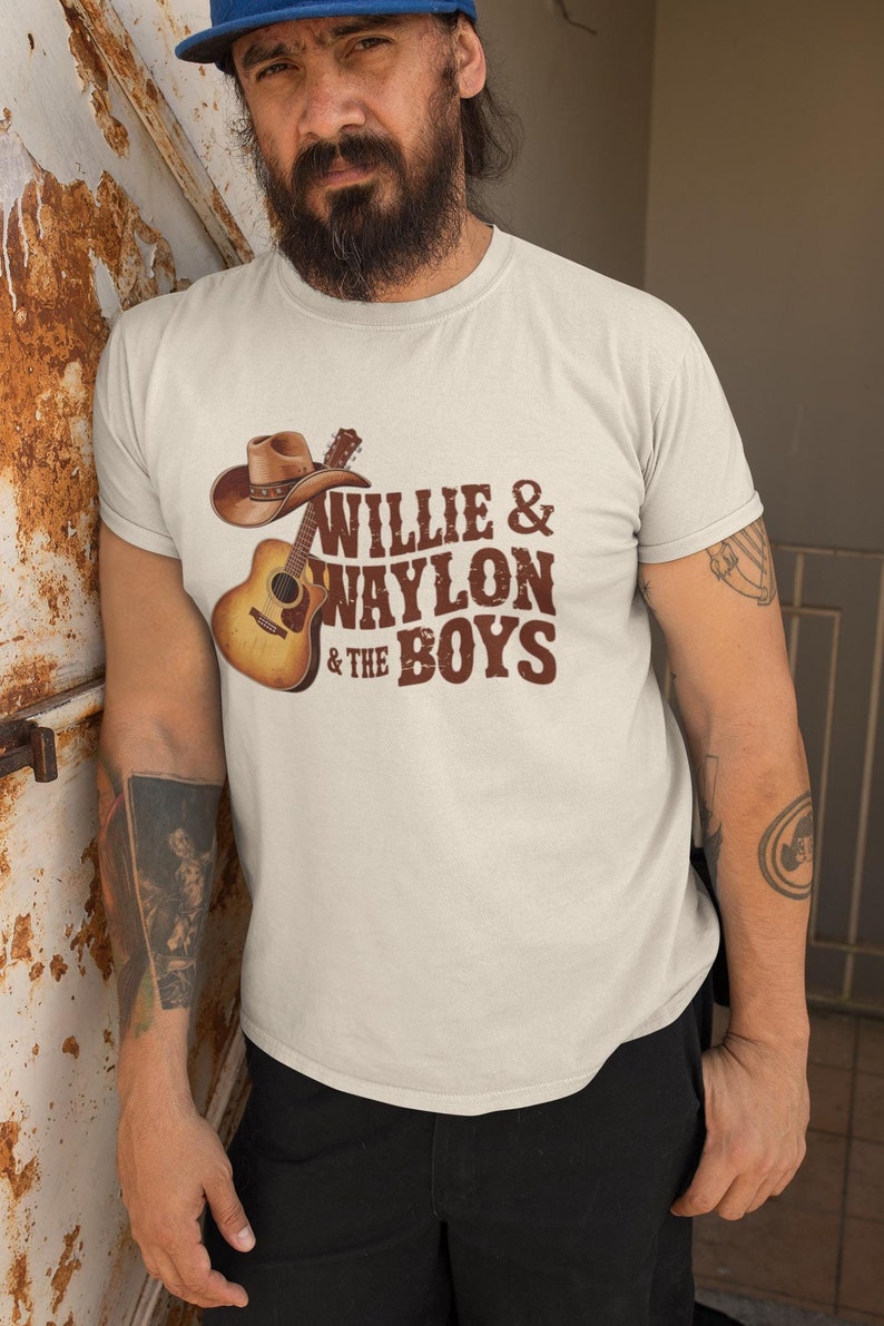 May include: A white t-shirt with a brown graphic of a guitar and cowboy hat. The text "Willie & Waylon & The Boys" is printed on the shirt.
