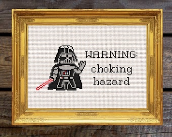 Può includere: Un ricamo a punto croce incorniciato con un personaggio di Darth Vader pixelato con una spada laser rossa e il testo "ATTENZIONE: rischio di soffocamento".