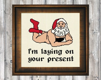May include: A cross-stitch pattern featuring a cartoon Santa Claus lying on his stomach with the text "I'm laying on your present".