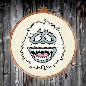 May include: A white, fuzzy, smiling snowman with a blue face and pink tongue. The snowman is in a circular embroidery hoop.