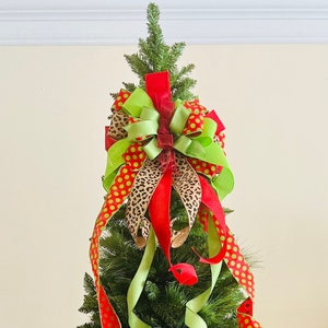 May include: A green artificial Christmas tree with a red, green, and leopard print bow on top.