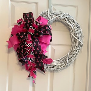 May include: A white twig wreath with a large pink and black ribbon bow. The ribbon is decorated with pink and black polka dots and pink ribbon with a black awareness ribbon design.
