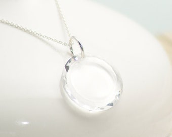 May include: A silver chain necklace with a clear crystal pendant. The pendant is round and has a faceted design.