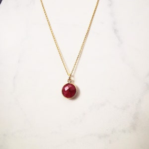 May include: A gold chain necklace with a red gemstone pendant. The pendant is round and has a faceted surface.