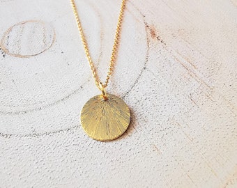 May include: A gold necklace with a round pendant. The pendant has a textured surface with a sunburst design.