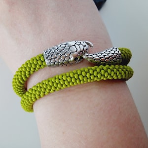 Puede incluir: Un brazalete de cuentas verdes con un cierre de cabeza de serpiente plateado.