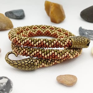 May include: A beaded snake bracelet in a gold, green and brown colour scheme. The bracelet is coiled and features a snake head charm at one end and a snake tail charm at the other end.