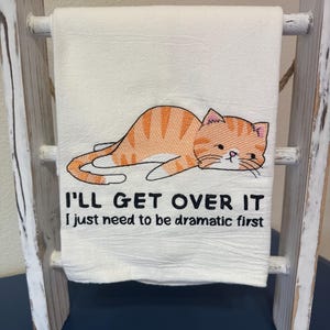 May include: White kitchen towel with an orange cat lying down and the text "I'll get over it I just need to be dramatic first."