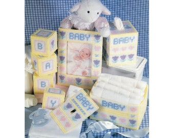 Pode incluir: Um conjunto de projetos de artesanato com tema de bebê, incluindo uma moldura de fotos, uma capa para caixa de lenços de papel, uma cesta para fraldas e blocos. Os projetos são todos feitos com tela amarela e branca e apresentam um design floral azul e rosa. Os projetos são decorados com a palavra "BABY" e alguns dos blocos têm letras.