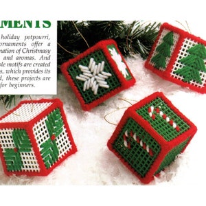 May include: Four red, white and green Christmas ornaments with different designs. The ornaments are cube-shaped and have a white background with red trim. The designs include a snowflake, a Christmas tree, a candy cane and a holly leaf.