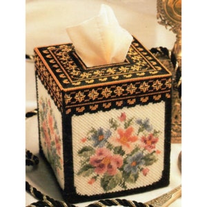 May include: A black and gold tissue box cover with a floral design. The flowers are pink, blue, and orange. The cover is made of needlepoint.