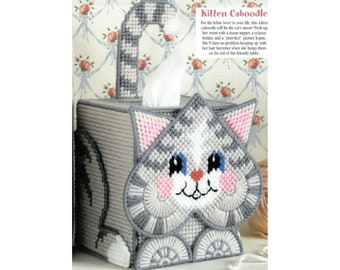 May include: Gray and white crocheted tissue box cover shaped like a cat with pink ears and a blue nose. The text "Kitten Caboodle" is above the cat.
