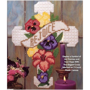 May include: White plastic canvas cross with a floral design and the word "Rejoice" on a banner. The cross is decorated with purple, pink, and yellow flowers. The cross is displayed against a wooden background with a purple candle.