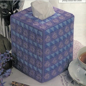 Op de afbeelding: Een paarse en blauwe tissueboxhoes met een geometrisch patroon. De hoes is gemaakt van garen en heeft een vierkante vorm.