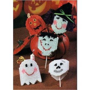 Pode incluir: Uma coleção de decorações de Halloween feitas à mão. A imagem apresenta uma abóbora, uma bruxa, Frankenstein, um fantasma e uma caveira, todos feitos de fio e montados em palitos. As decorações são em tons de laranja, preto, branco e verde.