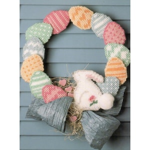 May include: A handmade Easter wreath with a white bunny in the center. The wreath is made of colorful plastic canvas eggs and a blue and gray bow.