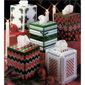 May include: Five Christmas-themed tissue box covers. The covers are made of white plastic canvas and feature different designs, including holly, stripes, plaid, and beads.